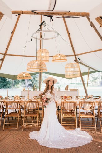 A beautiful bride stands under a huge tipi at her wedding. There is a beautifully styled table behind her.
