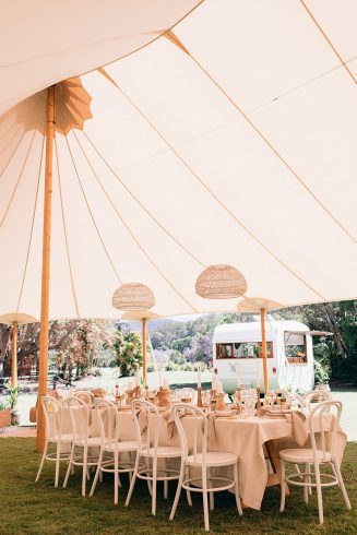 A shot underneath a huge tipi ready for a tipi wedding. A large table is styled featuring florals and white bentwood chairs.
