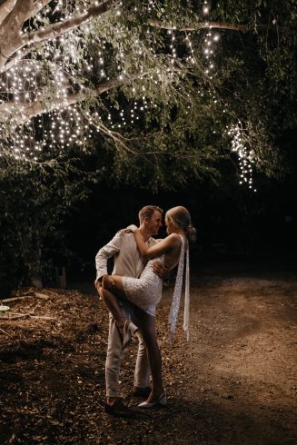 Bride + groom kissing under tree with fairy lights